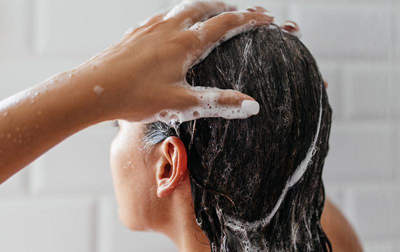 Eine Person mit langen dunklen Haaren wäscht sich diese mit Shampoo.