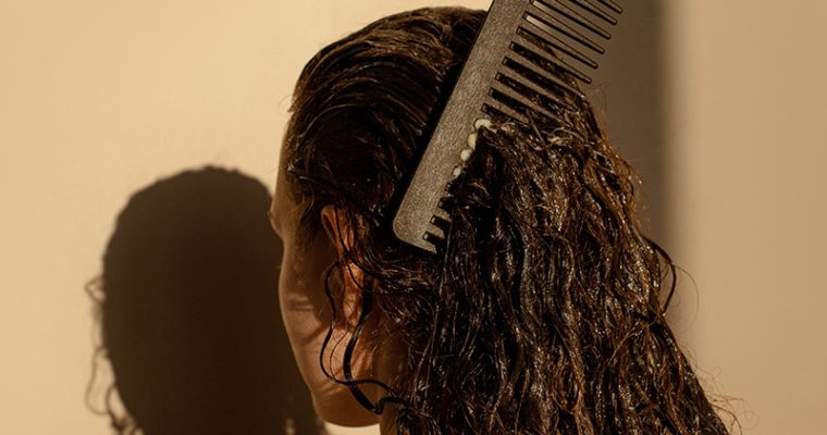 Eine Person mit nassen, langen braunen Haaren kämmt sich durch die Haare.